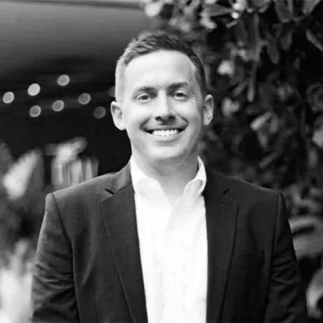 A smiling portrait of Kevin J. Buxton, Managing Director of Southpaw Capital, wearing a suit standing outdoors with blurred string lights and foliage in the background.