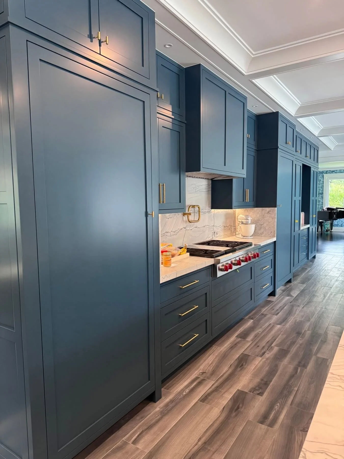 Modern kitchen with navy blue cabinets, marble backsplash, wooden drawers, and stainless steel appliances, with a window and hardwood flooring.