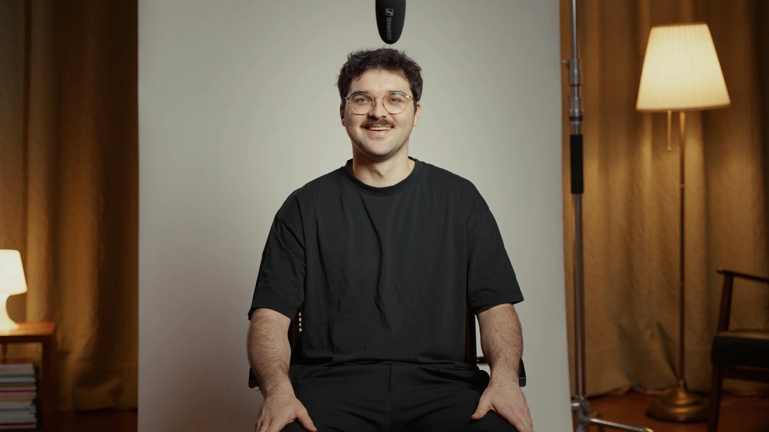 Junger Mann mit Brille sitzt vor einem weißen Studio Hintergrund, während eine Tonaufnahme aufgenommen wird.