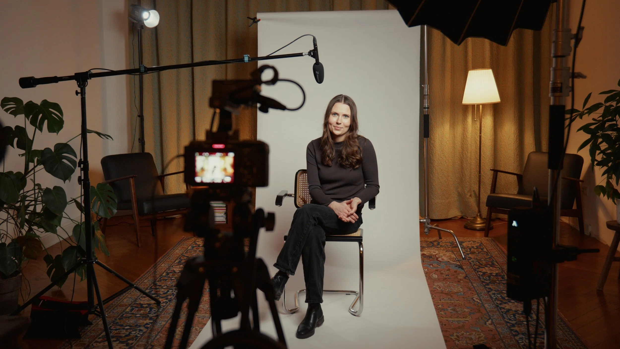 Frau sitzt vor einem weißen Hintergrund in einem Fotostudio, umgeben von Licht- und Kameraausrüstung.