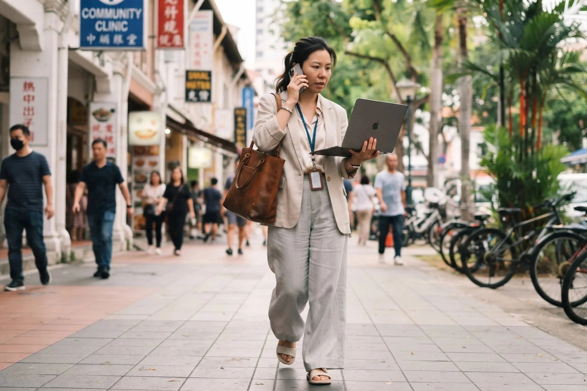 A Chinese female counsellor multitasking with a laptop and phone while walking on a Singapore street