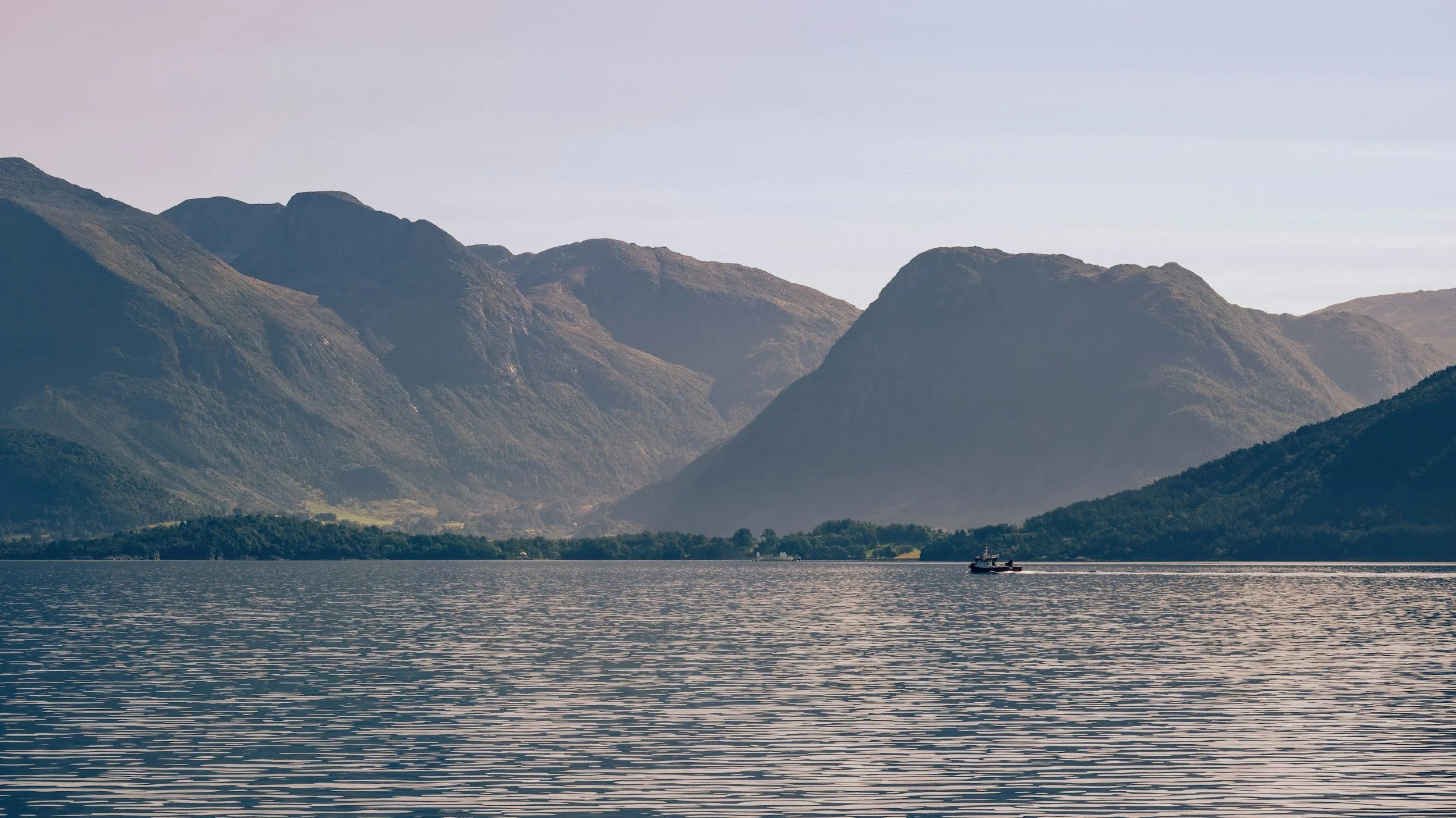 A lake with a small boat and mountainous landscape in the background under a clear sky.