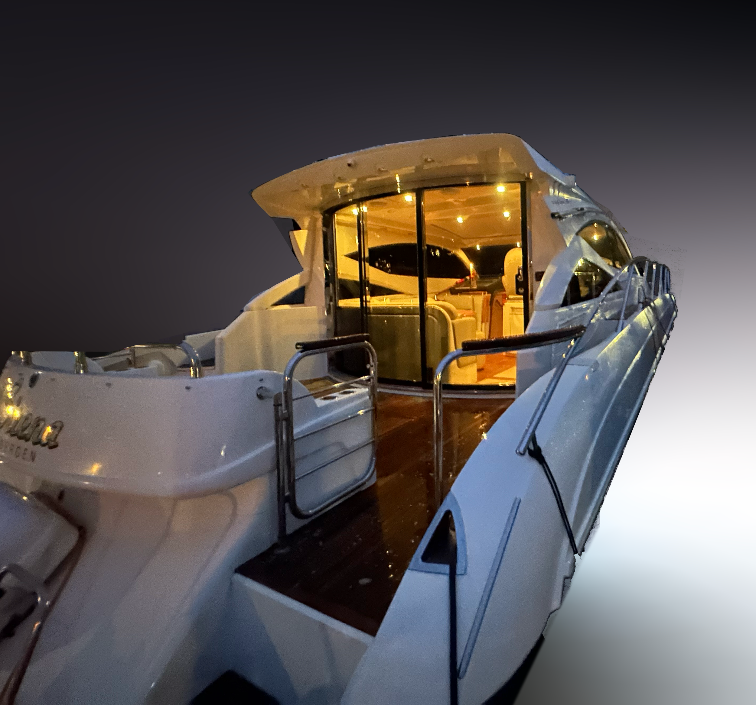 Nighttime view of a luxury yacht with illuminated interior bar area, modern design, and outdoor deck with railings.