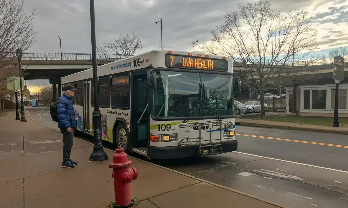 An image of a bus that is parked at the stop. A white man is on the sidewalk waiting.