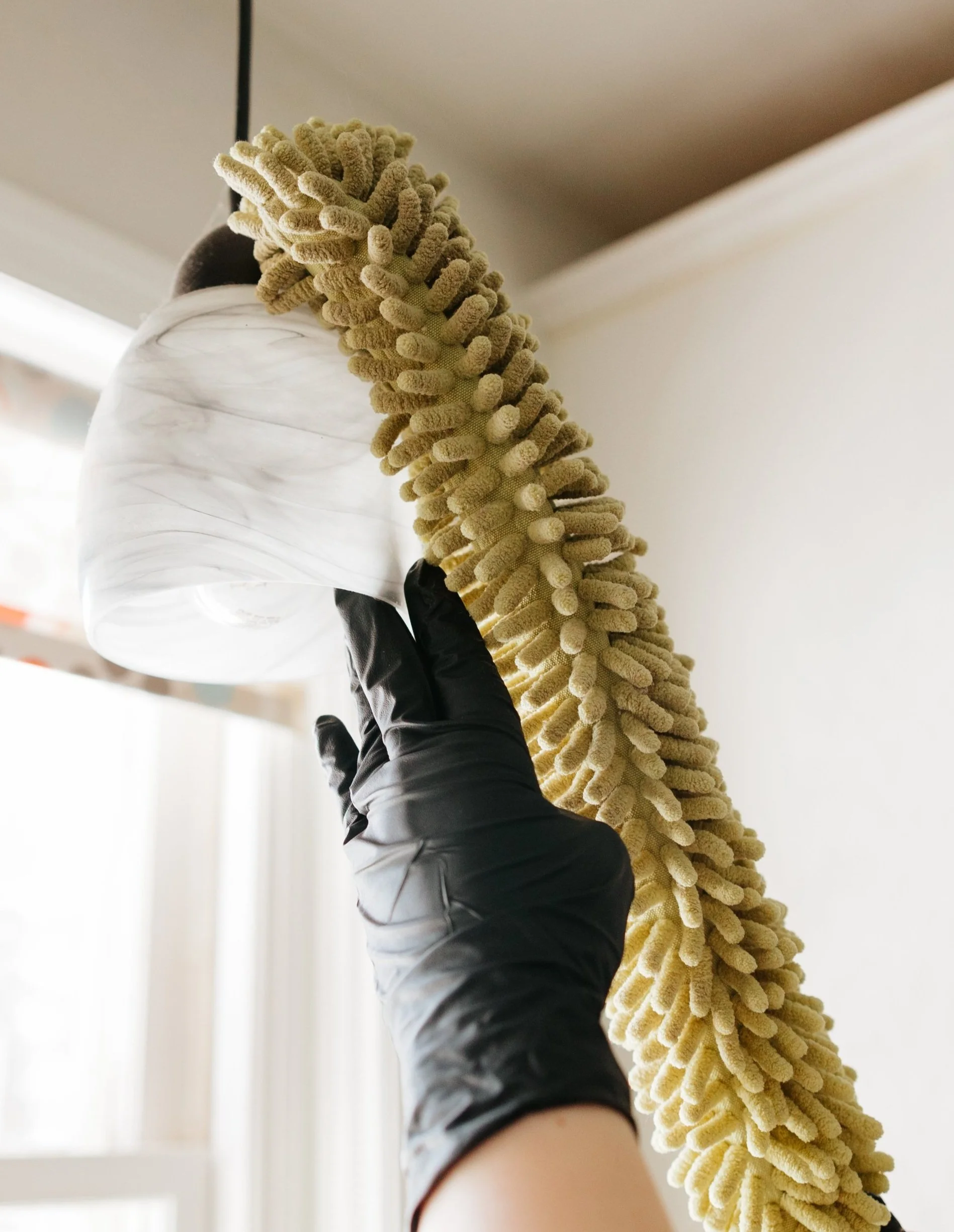 A person wearing a black glove holding a duster in front of a ceiling.
