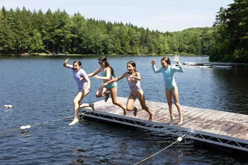 Four kids jumping off the lake dock in swimming class