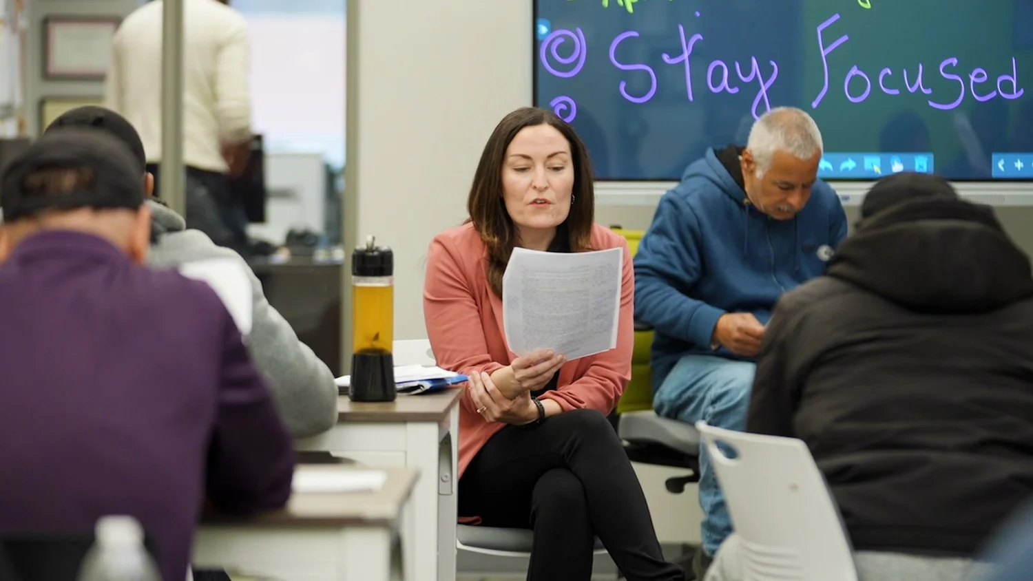 A People & Stories coordinator reads a printed short story aloud to participants seated in a discussion circle