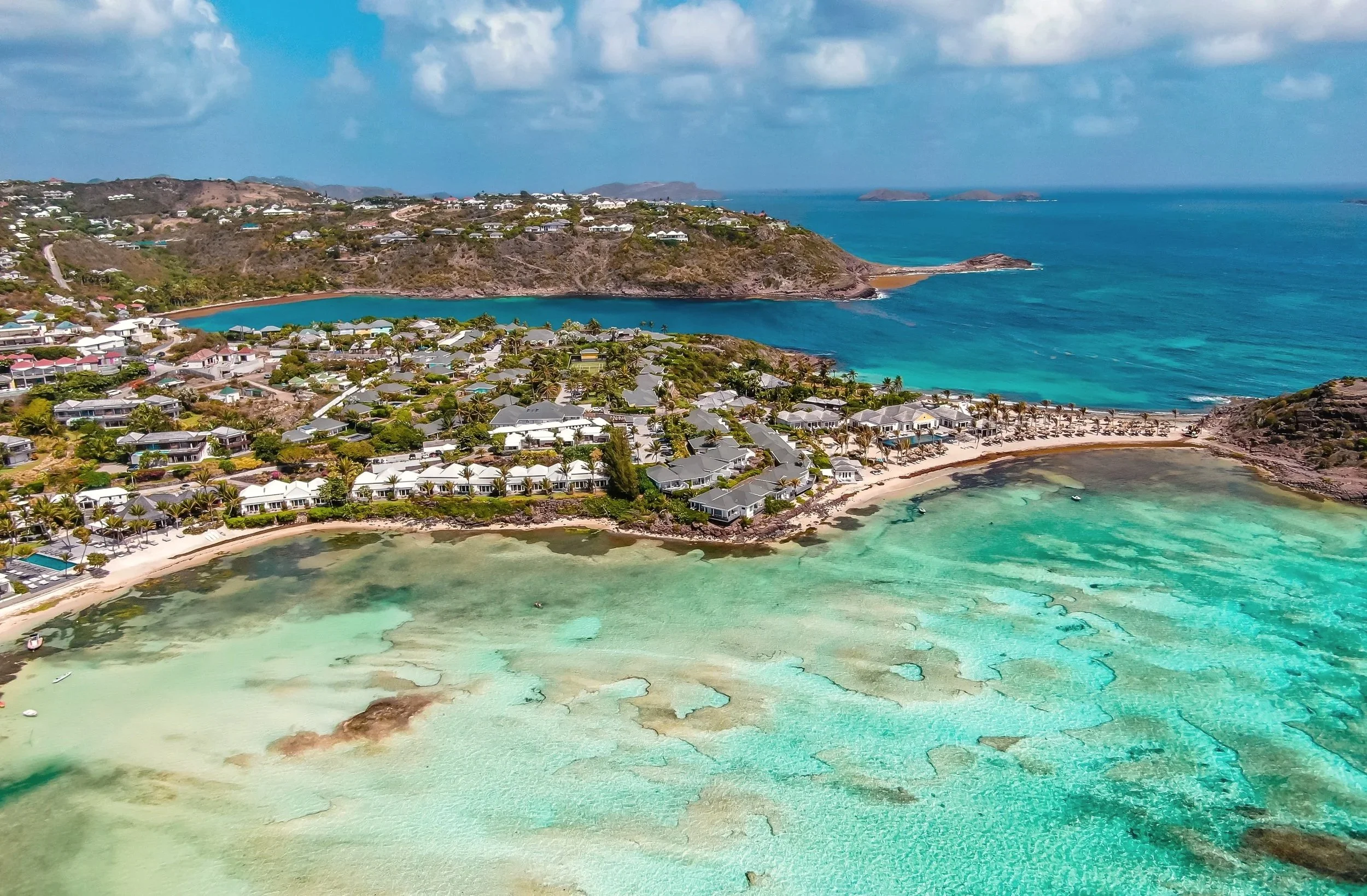 Aerial view of a coastal neighborhood with white houses, palm trees, sandy beaches, and turquoise waters in a tropical setting.