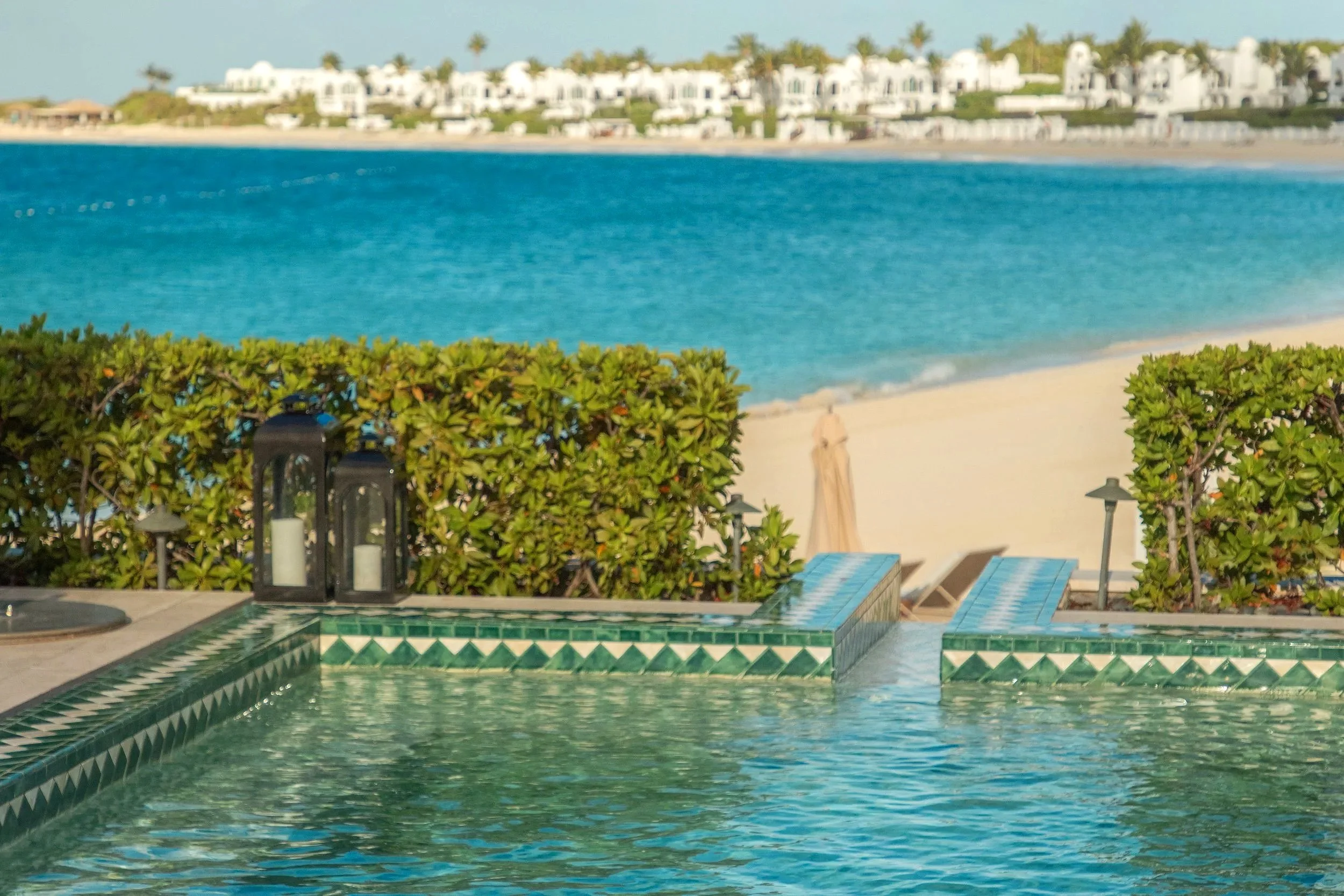 Woman in a red dress standing by a small pool overlooking the ocean, with greenery and a white railing nearby.