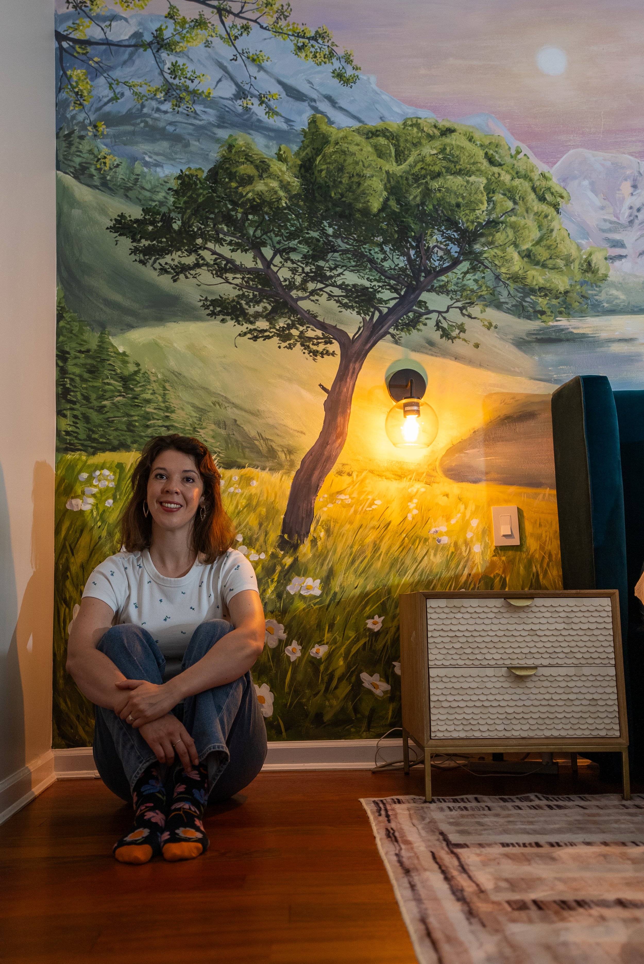 Martha Antonelli sitting in low lighting cosy bedroom in front of mural