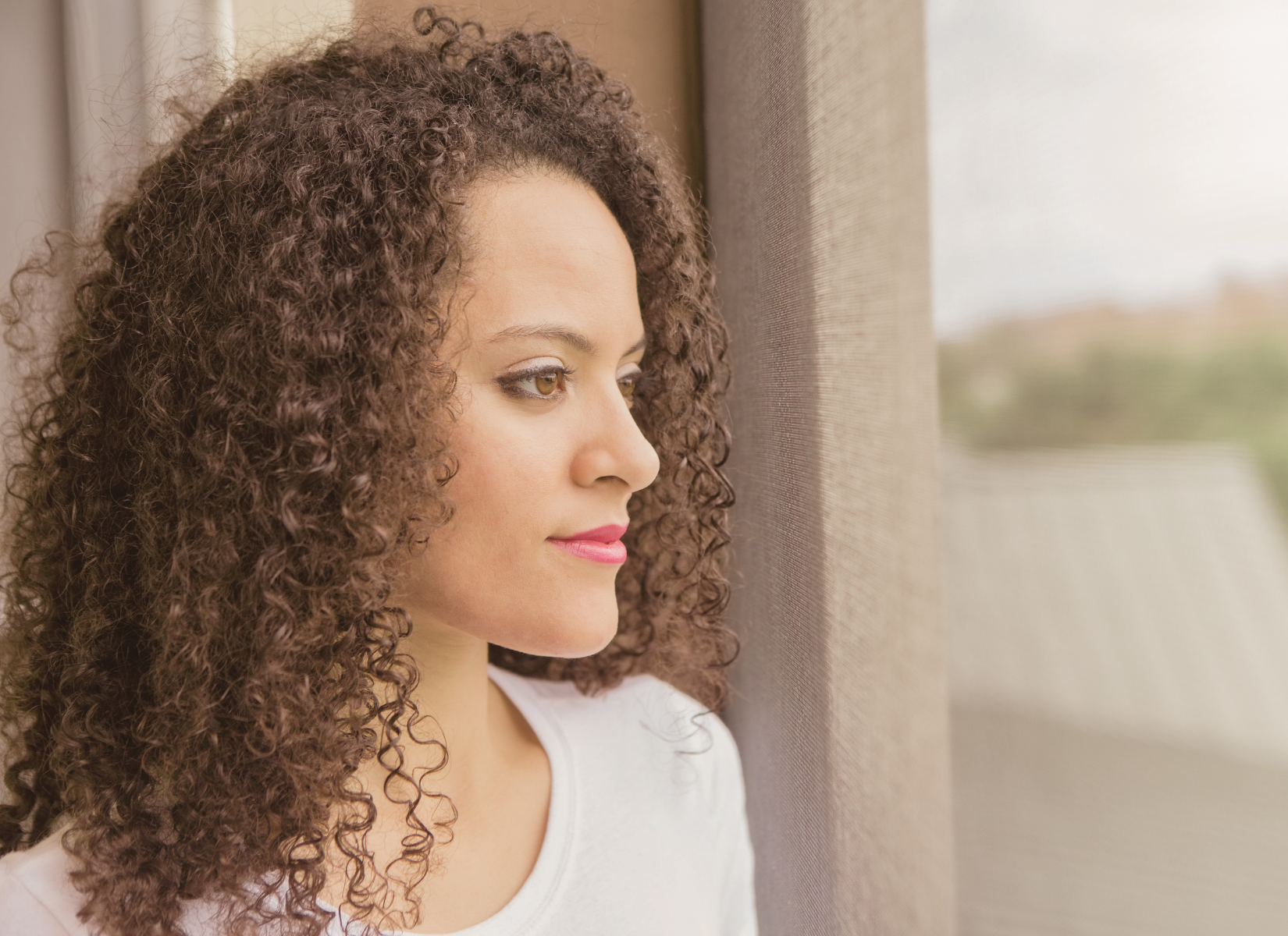 BIPOC Woman standing by a window and looking outside