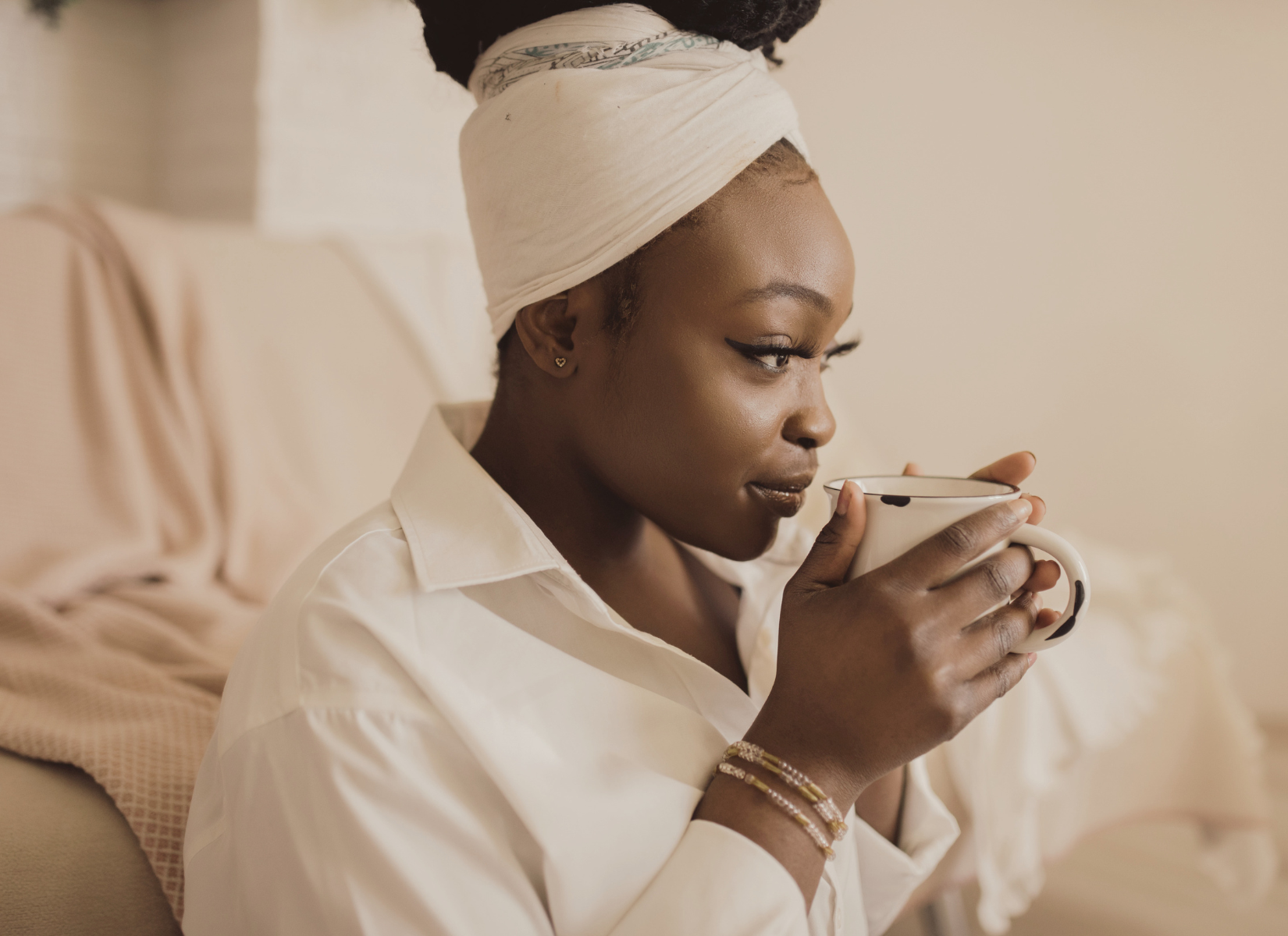 BIPOC Person holding a mug and gazing thoughtfully to the side in a softly lit room.