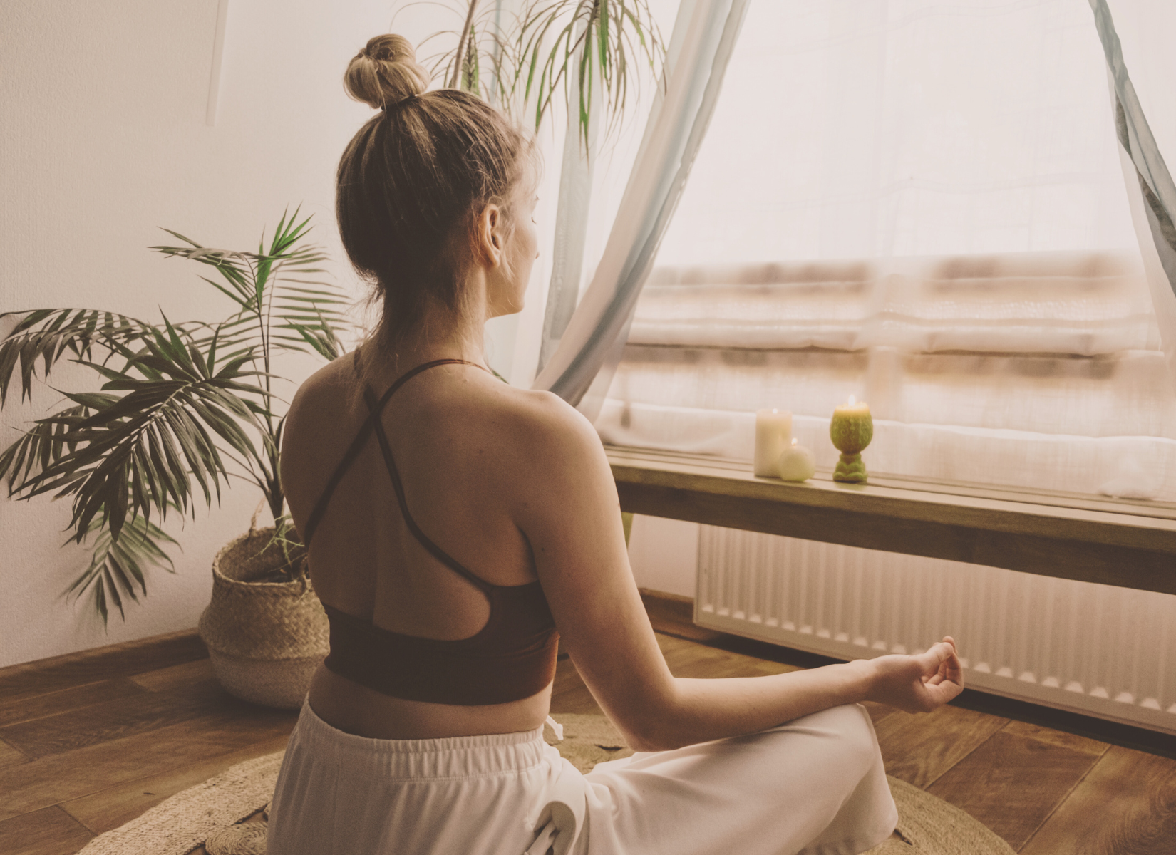 Mindful women amidst candles & plants, meditating in a sunlit room