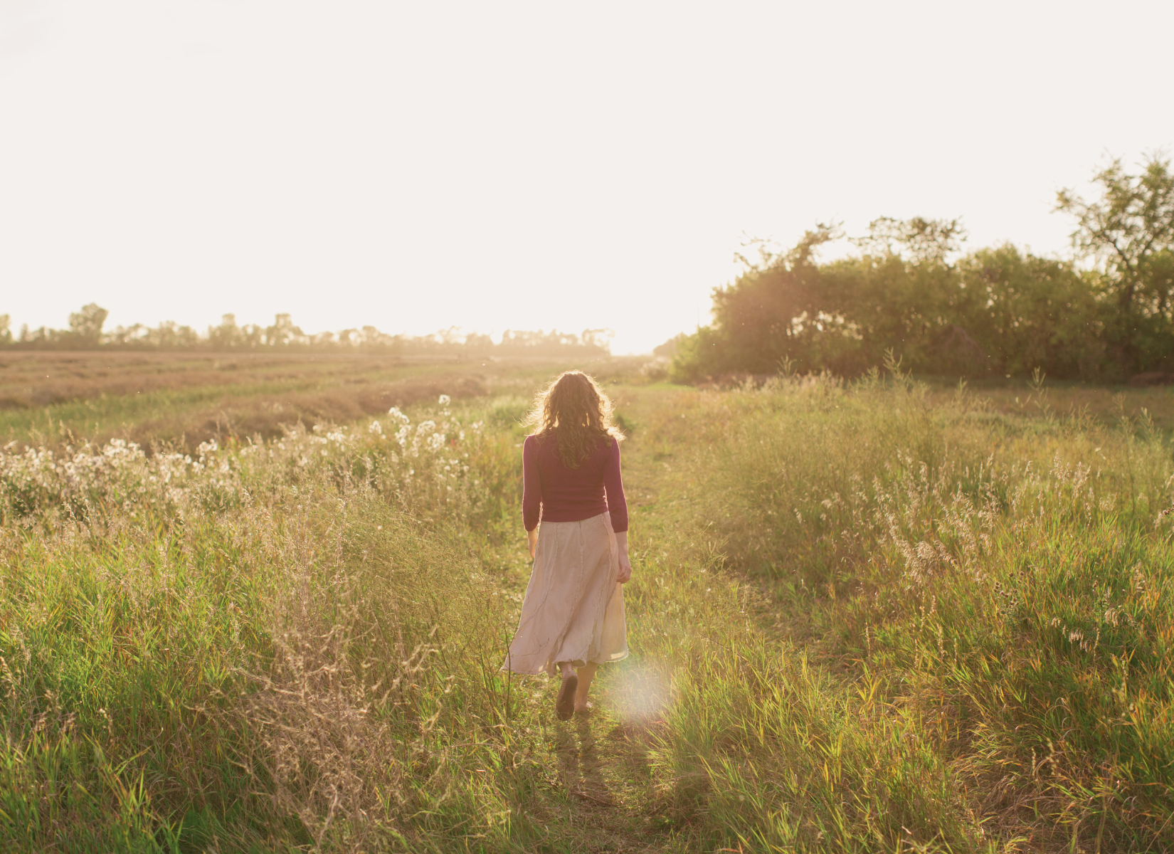 Person walking along a grassy path in warm evening sunlight.