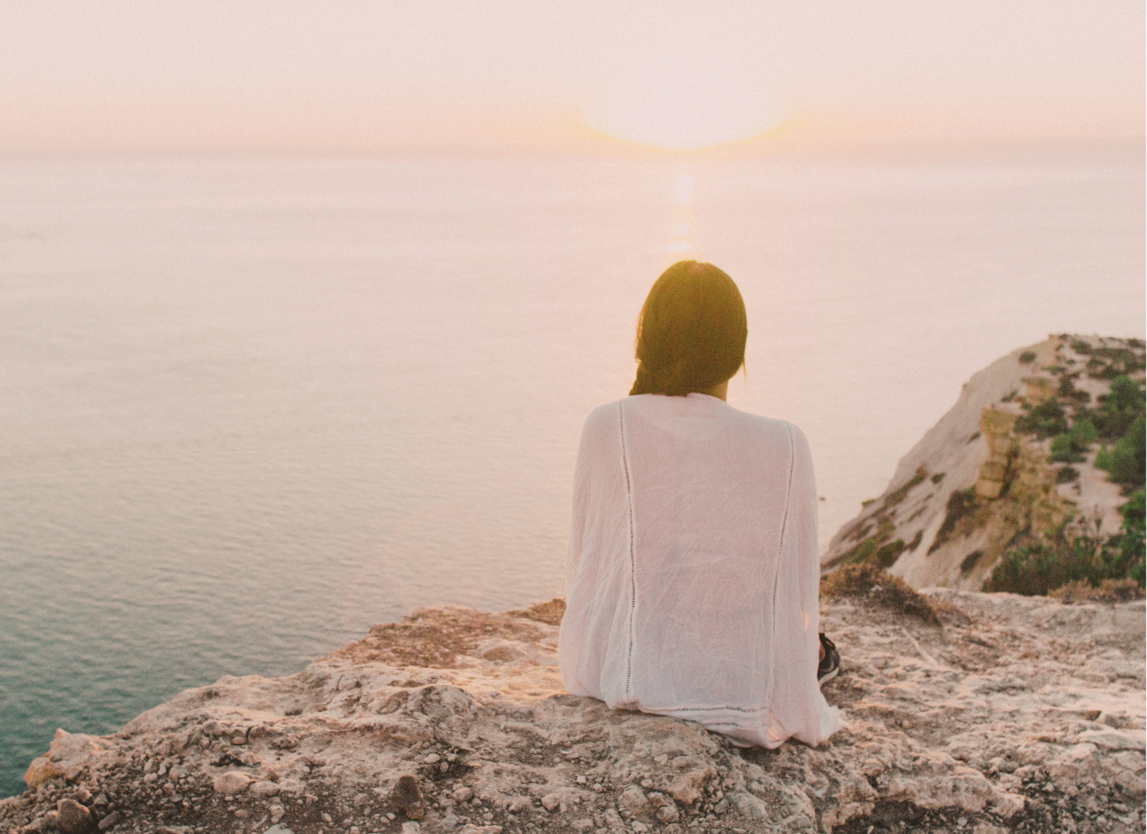 Person sitting on a rocky overlook and looking out across the water.