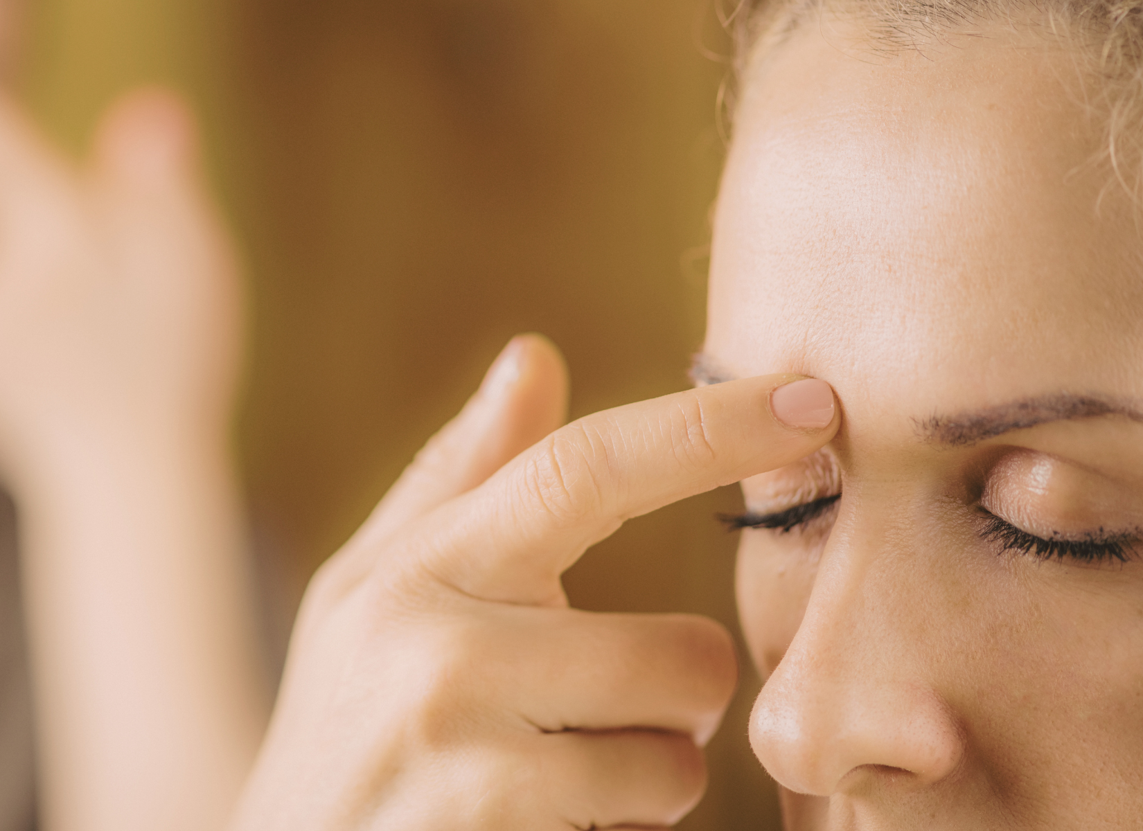 A woman gently tapping acupressure points on her face using Emotional Freedom Technique (EFT) to relieve stress and anxiety in a calming environment.