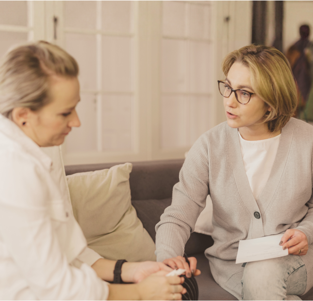 Woman sitting on a couch with her eyes closed while holding another person's hand during a therapeutic mindfulness exercise.