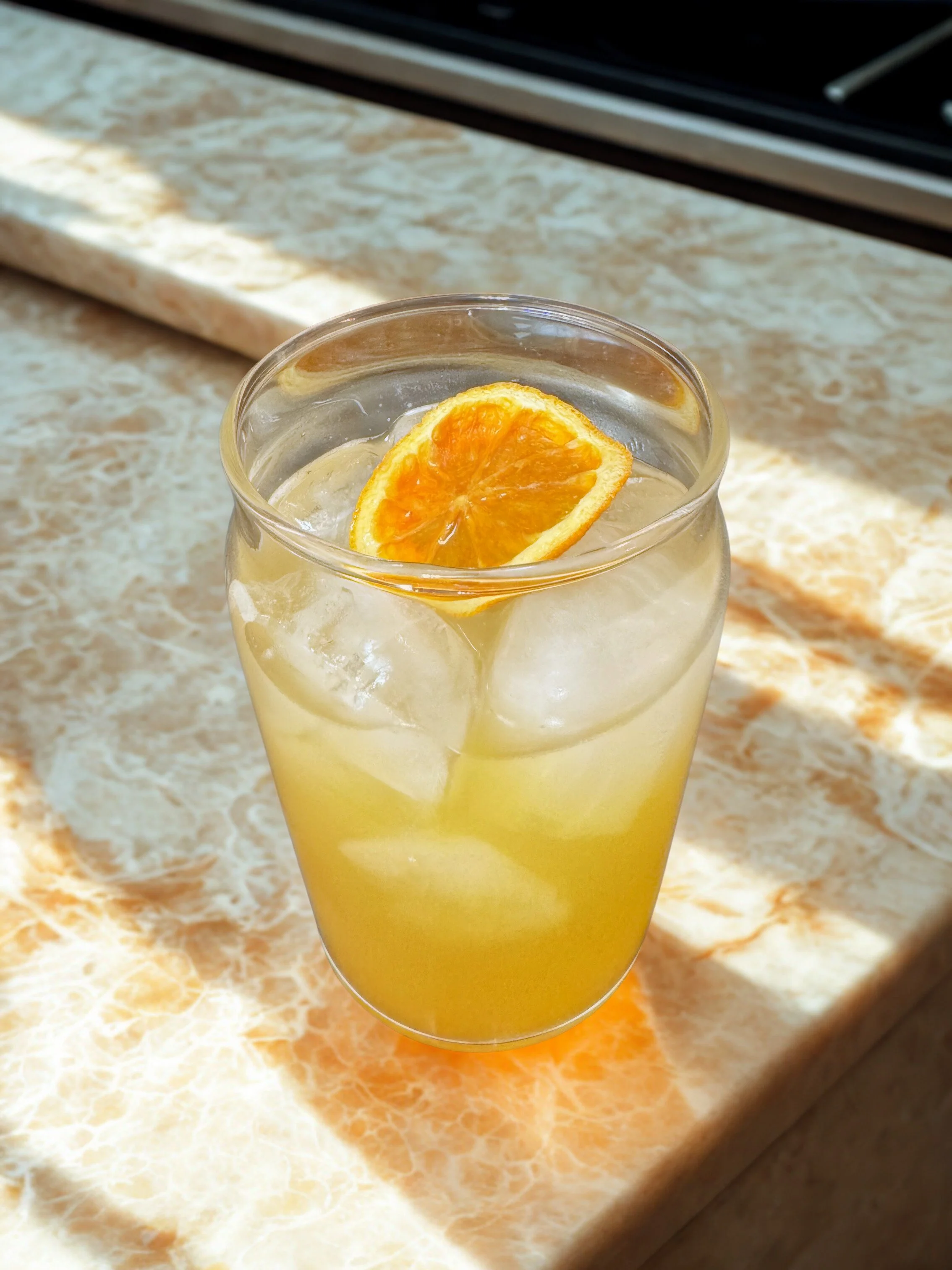 glass with ice cubes and allergy palmer drink of lemon, nettle, and honey with orange slice garnish on marbled counter