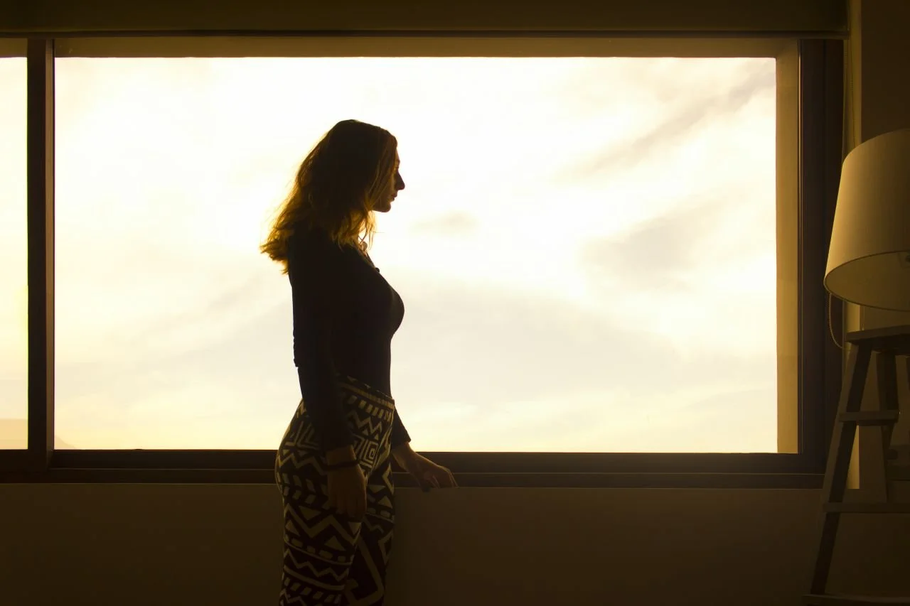 woman-in-black-long-sleeve-shirt-and-tribal-leggings-standing-by-the-window-during-daytime