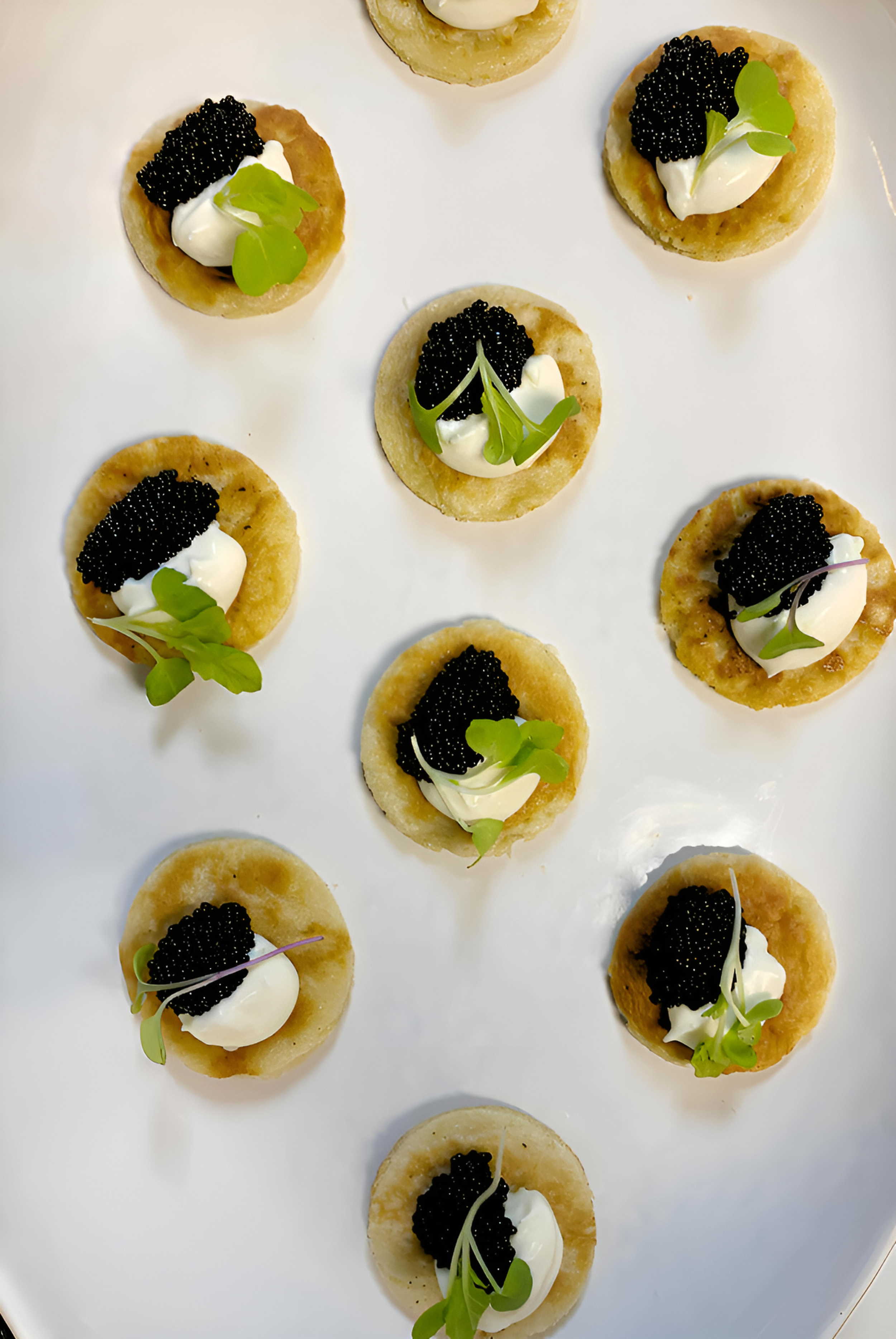 Blini topped with crème fraîche, caviar and microgreens served as passed hors d’oeuvres at an Eliza private event