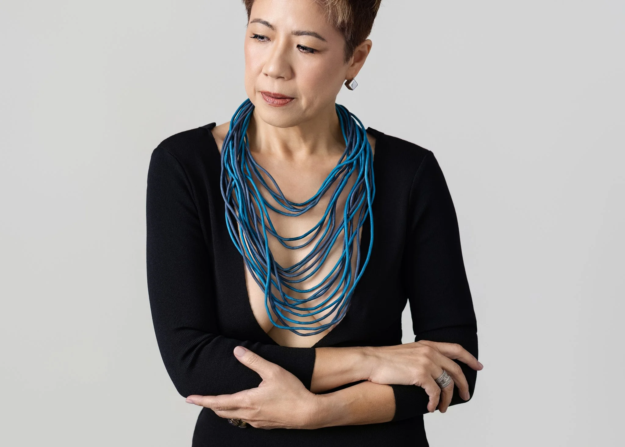 Asian woman looking left. Wearing a low cut black dress with a turquoise multi-string necklace 