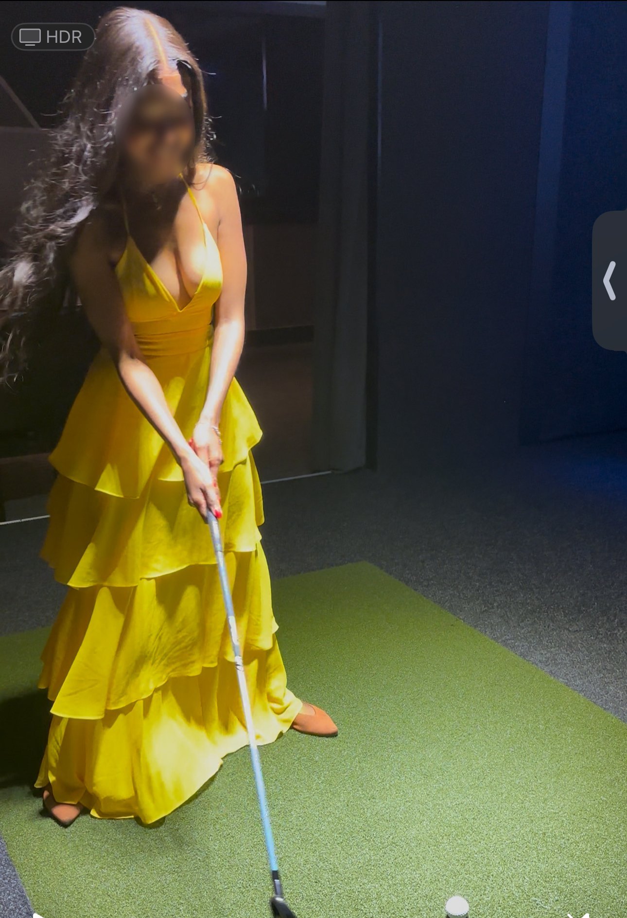 Woman in a yellow dress practicing golf on an indoor green.