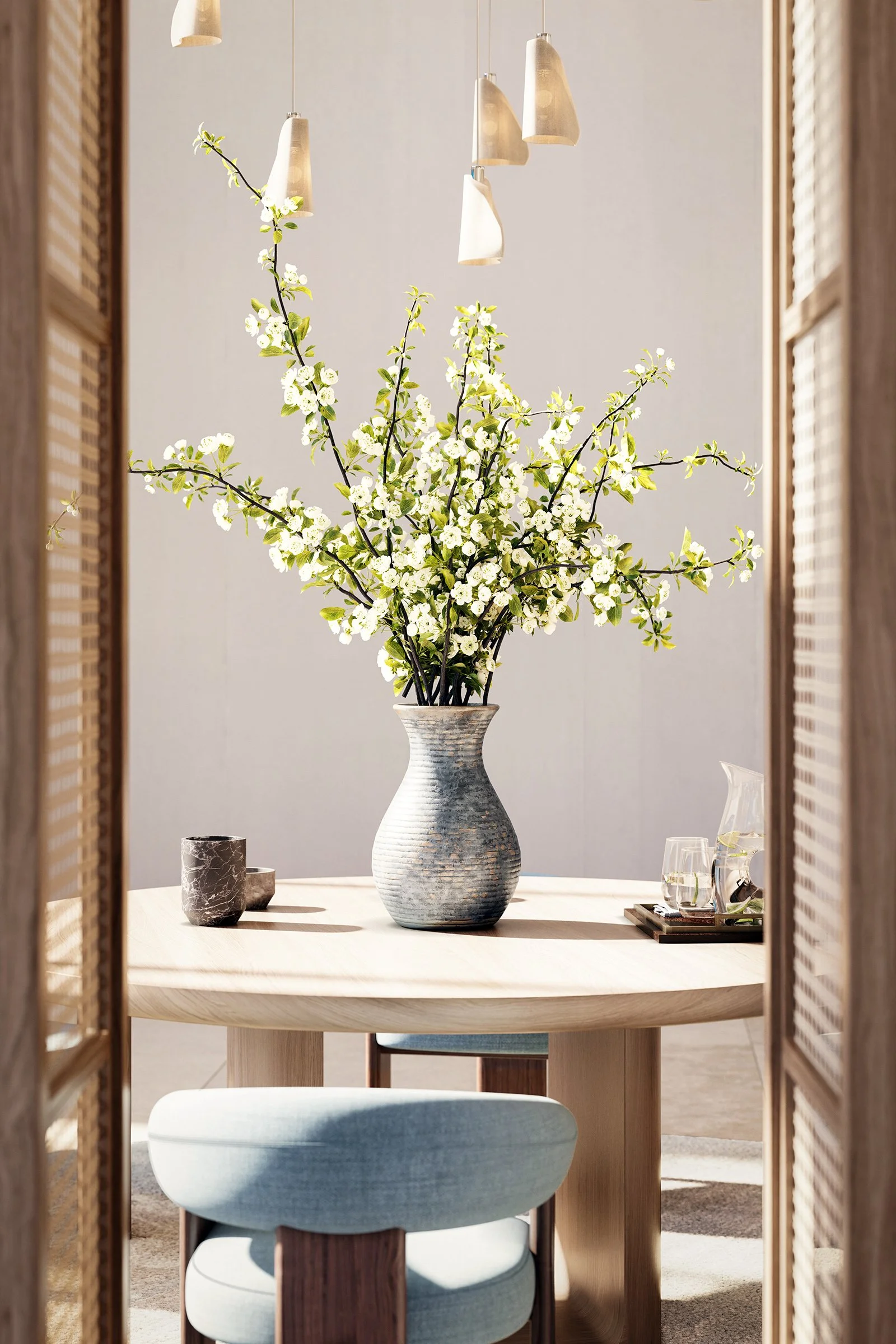 A vase with white flowering branches on a round dining table, with a decorative cup and glasses nearby, viewed through sliding wooden door panels with woven design, in a modern interior setting.
