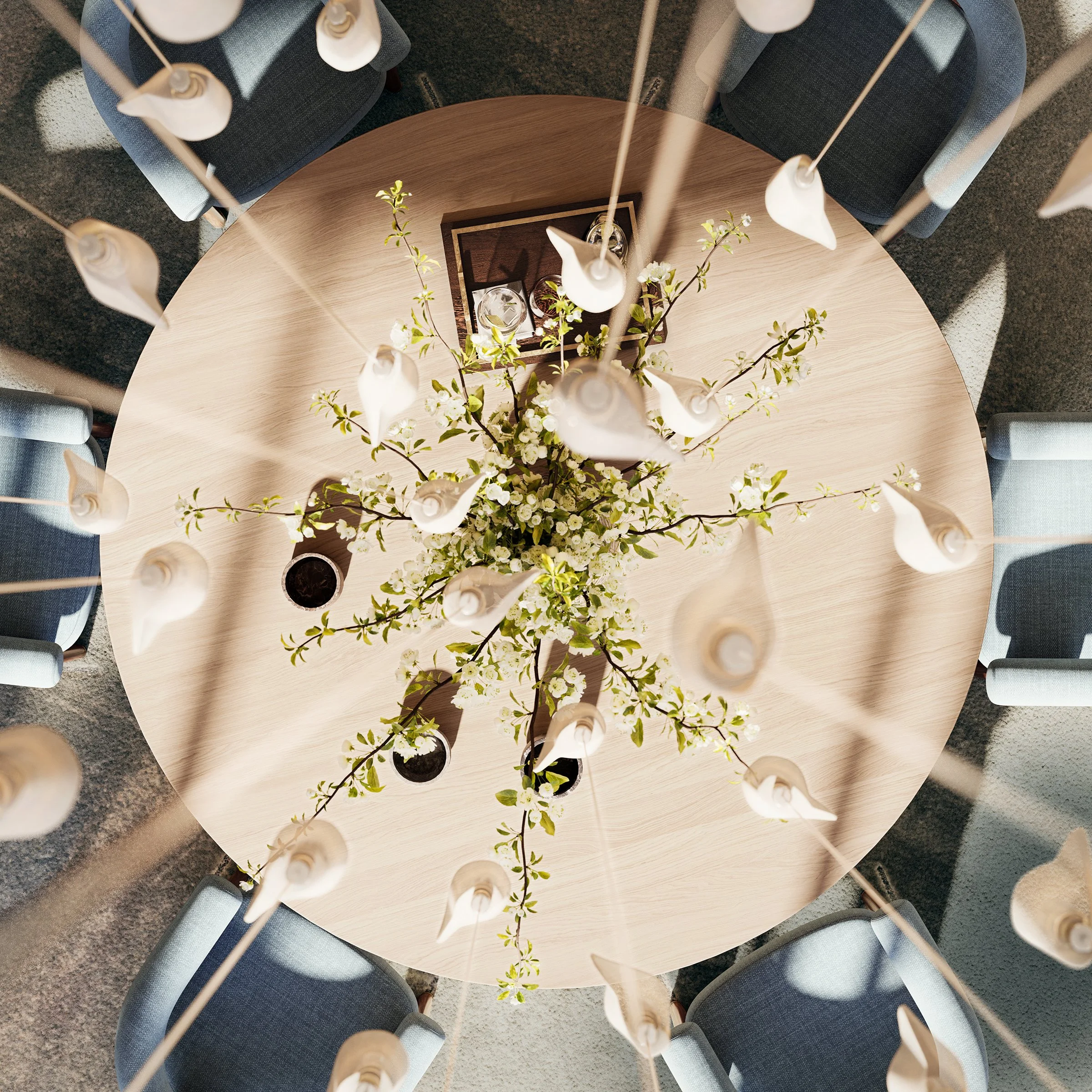 A top-down view of a round wooden table surrounded by four navy upholstered chairs with wooden legs, decorated with a vase of white flowers and surrounding candle holders with unlit candles.