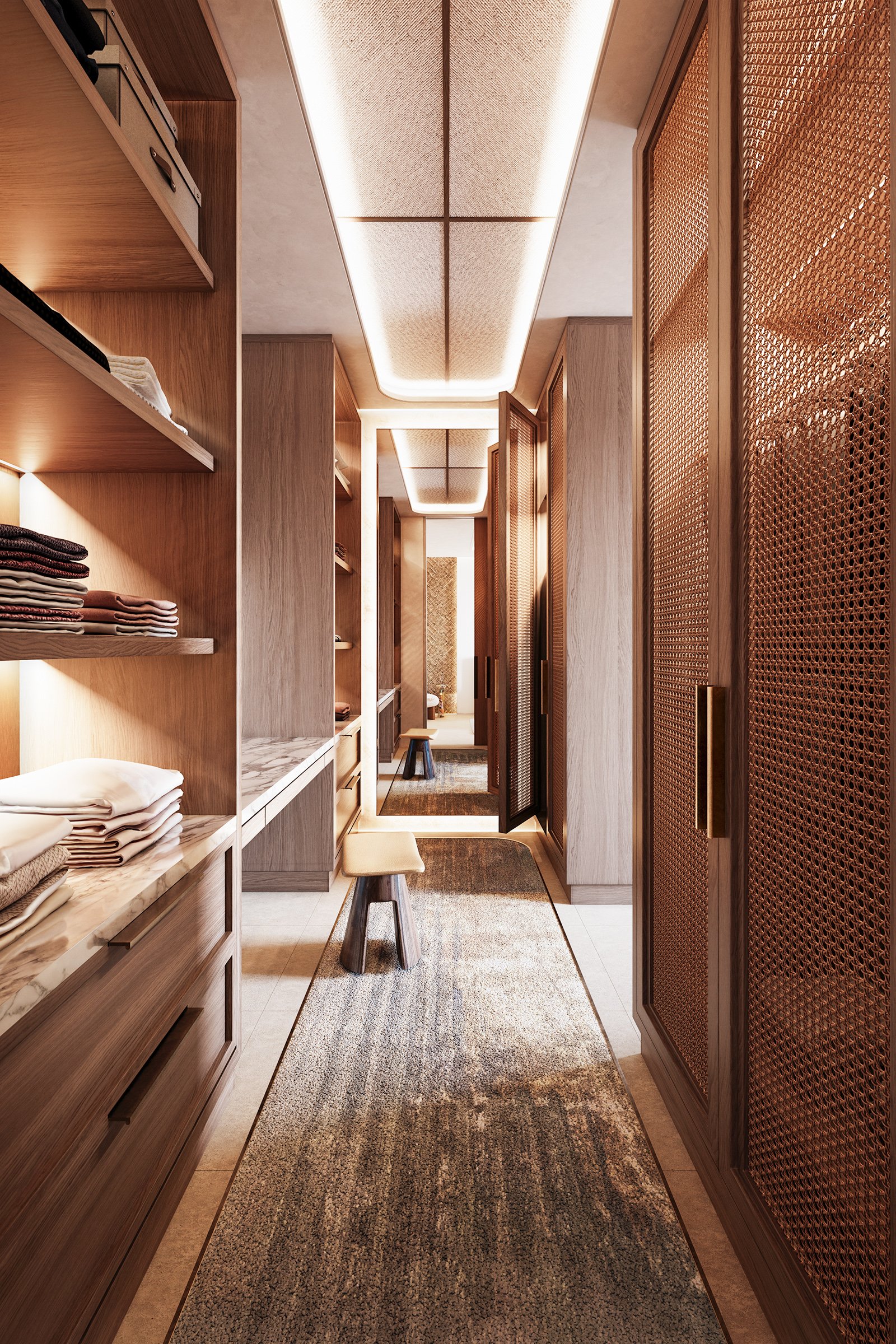 A narrow walk-in closet with wooden shelving on the left holding folded clothes and towels, a small beige stool, and decorative textured wooden doors on the right, with soft warm lighting and a carpeted floor.