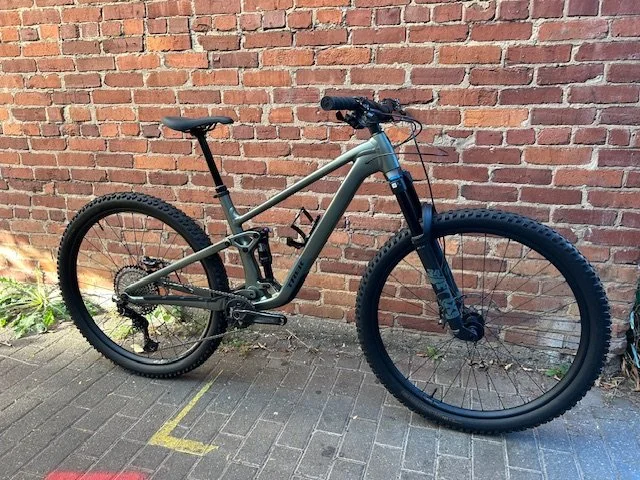 Gray mountain bike with thick tires leaning against a brick wall on a sidewalk.