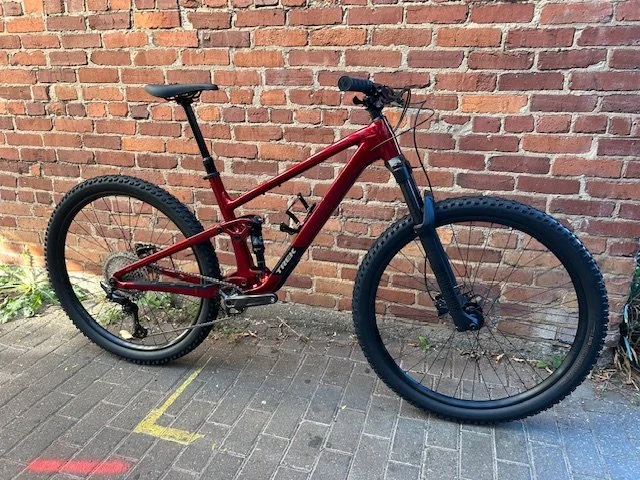 A red mountain bike with black tires parked on a gray brick sidewalk against a red brick wall.