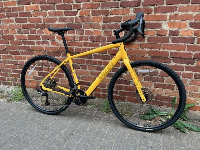 Yellow Salsa mountain bike leaning against a brick wall on a sidewalk.