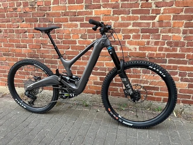Electric mountain bike with a matte black frame, thick off-road tires, and a brick wall background.