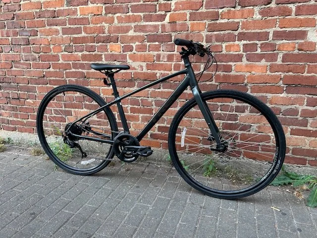 Black bicycle leaning against a brick wall on a sidewalk.