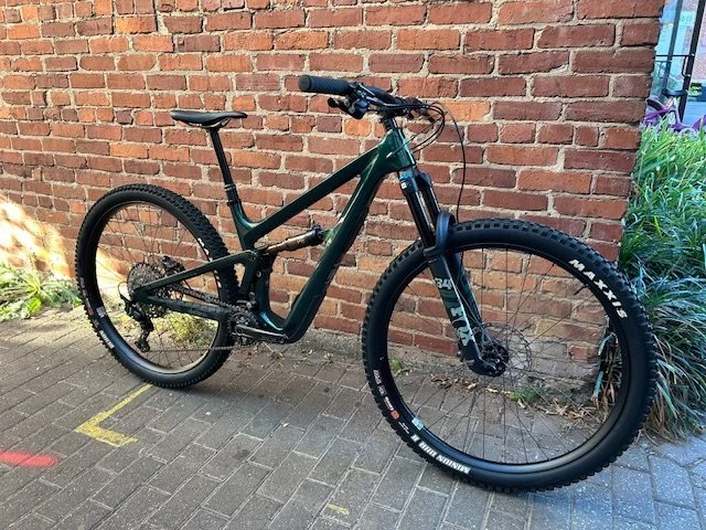A black and green mountain bike leaning against a brick wall outdoors.