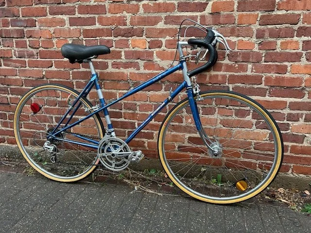 A blue bicycle leaning against a red brick wall.
