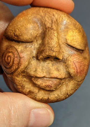 Hand holding a small sculpted clay face used for a handmade spirit doll.