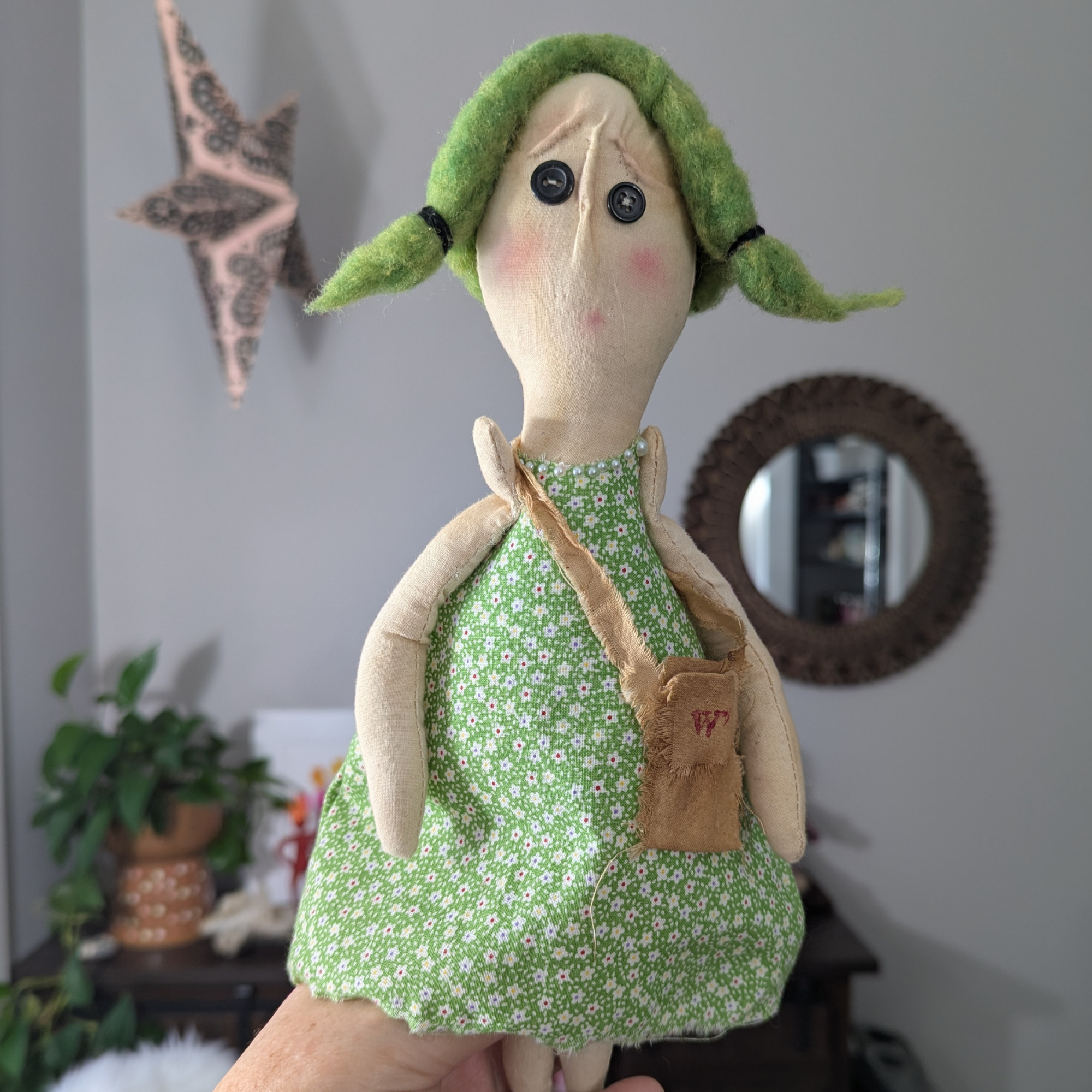 Handmade worry doll with green dress, button eyes, and small fabric pouch, held in someone’s hand.