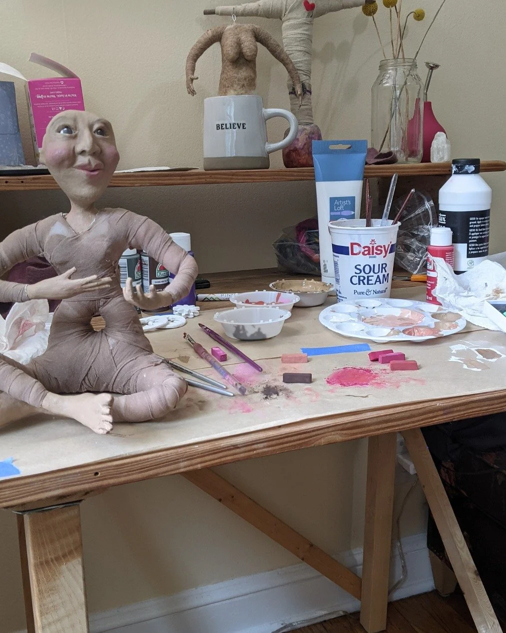 This is what the middle of making looks like.

Pastels, paint, a sour cream container full of brushes, and a doll who's starting to have opinions about how this is going.

This is the stage I love most, when she's not finished but you can already fee