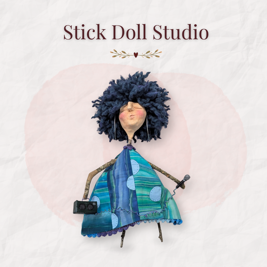 Handmade stick doll with wild dark blue yarn hair, a blue and turquoise fabric dress, and tiny microphone and speaker details beneath the words “Stick Doll Studio.”