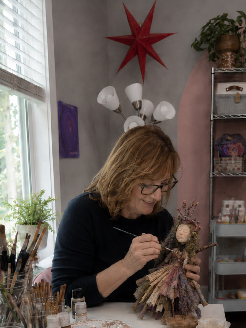 Woman painting the face of a handmade stick doll during a private creative retreat in a cozy Asheville art studio.