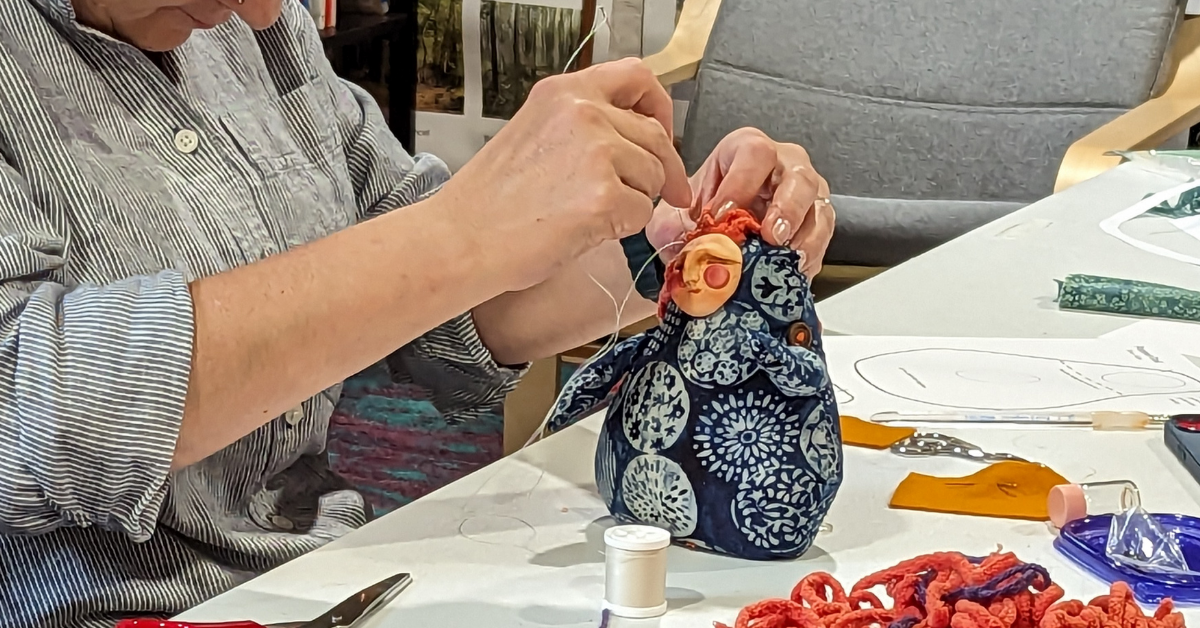 A woman sewing and assembling a handmade spirit doll during a small studio workshop.
