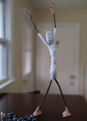 Spirit doll armature with raised arms made from sticks, wire, and wrapped fabric.
