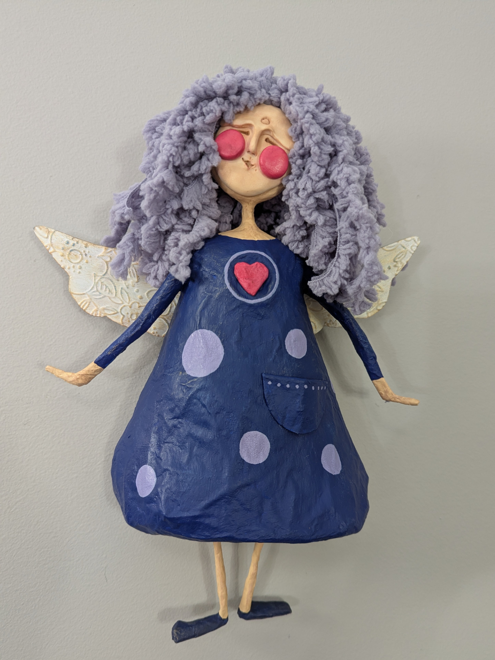 Finished papier-mâché angel with lavender yarn hair, textured wings, and a blue painted dress.