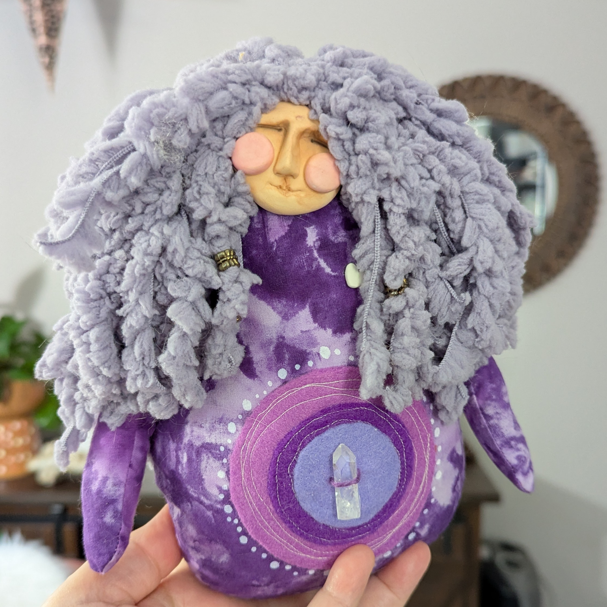 Handmade poppet doll with a felted face, curly purple yarn hair, and a stitched crystal detail on the belly.