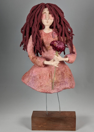 Handmade spirit doll with long yarn hair holding a flower, mounted on a wooden base