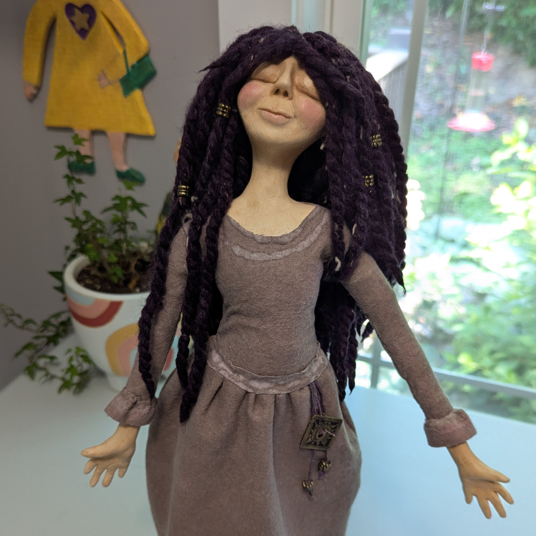Finished handmade spirit doll with long purple yarn hair, a mauve dress, sculpted hands, and a small decorative charm at her waist.