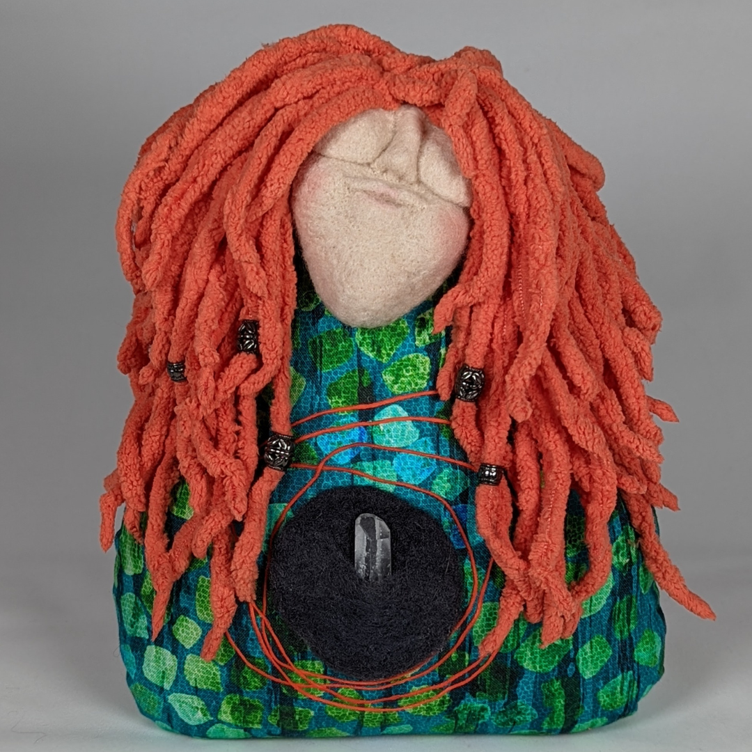 Handmade spirit doll with red yarn hair, a green patterned body, black heart, and small crystal at the center. Made by Stacy Vajta