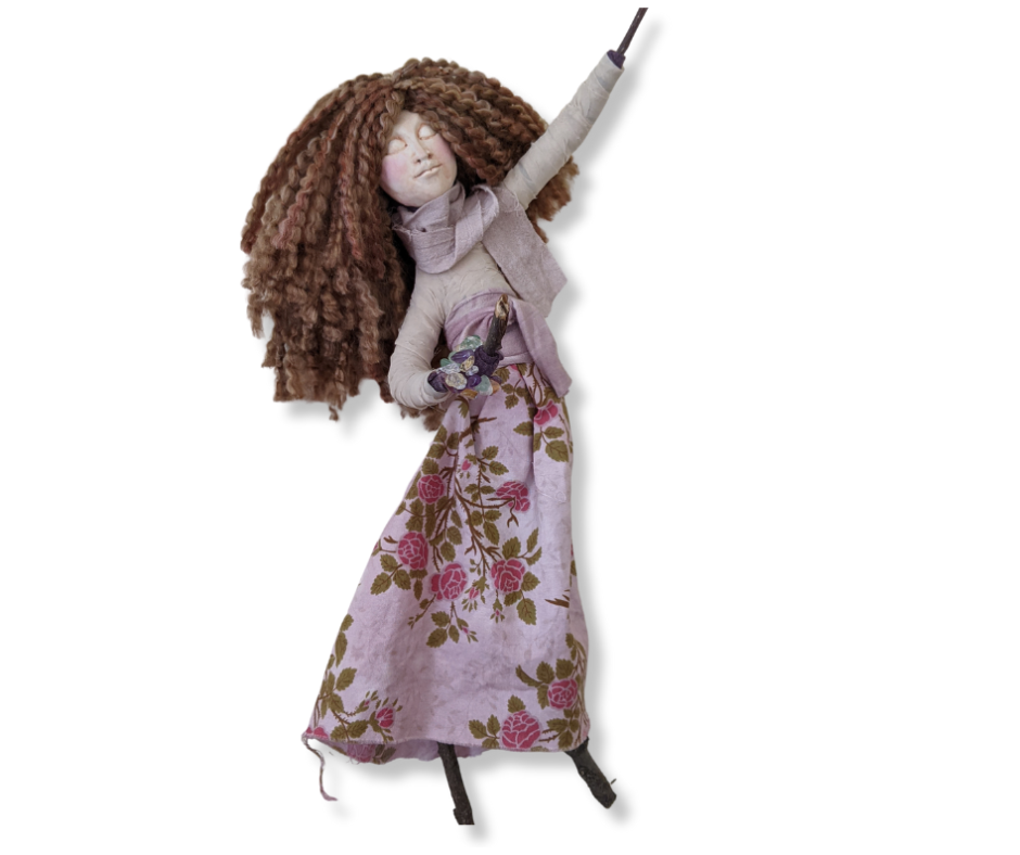 A playful stick doll posed like a dancer, with flowing brown hair, a flower petal skirt, a scarf, and a free-spirited 1970s vibe.