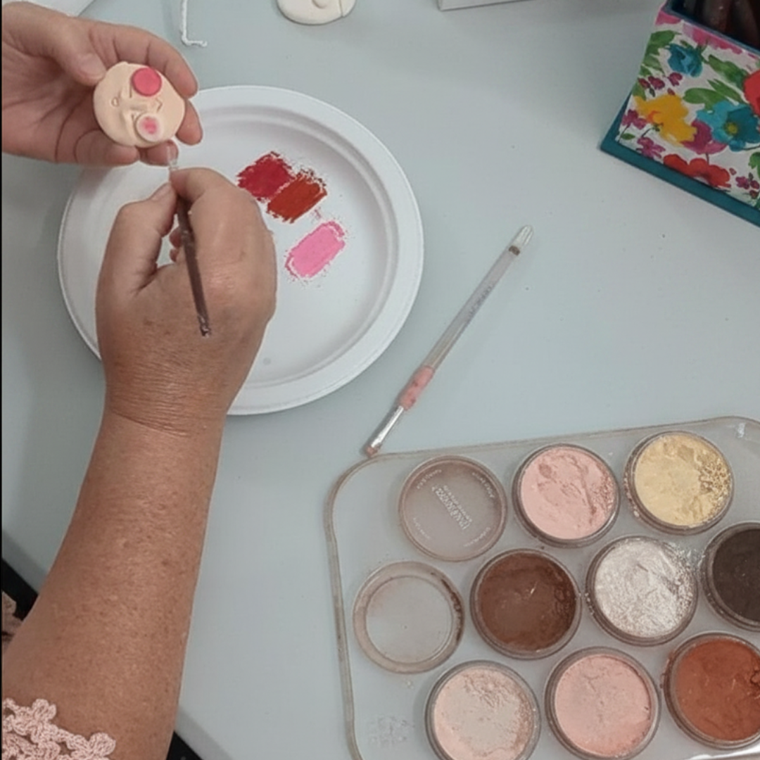 Hands painting rosy cheeks on a small clay angel face for a papier-mâché angel workshop.